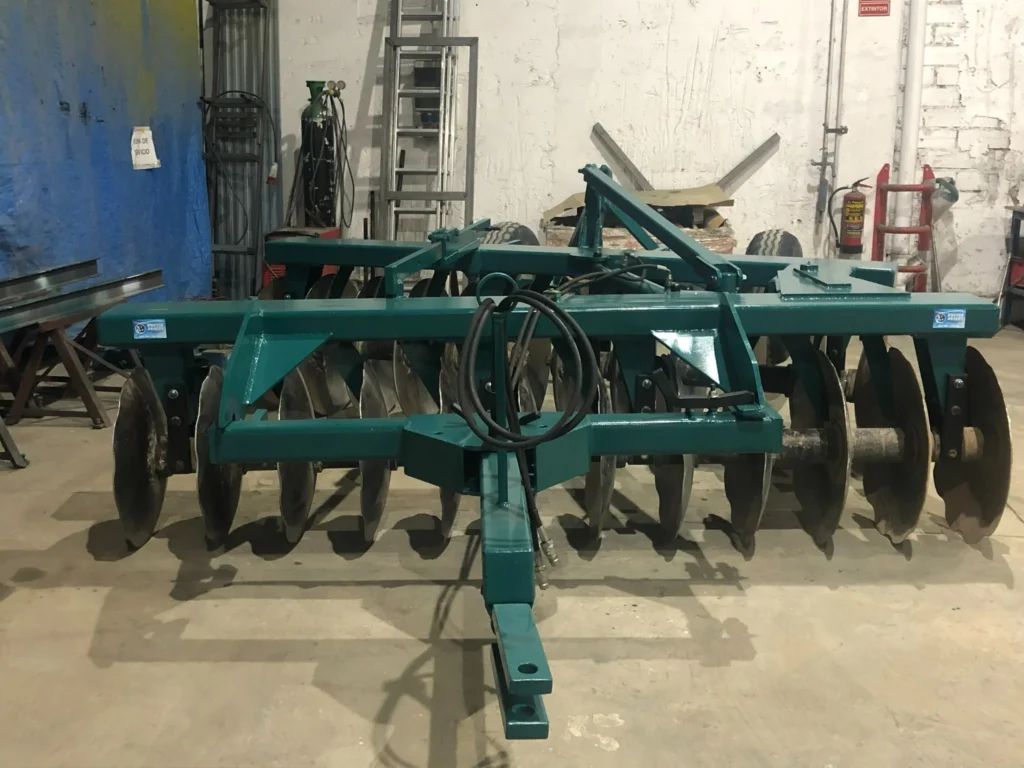 Vista frontal de un arado de discos metálico pintado de verde, ubicado en el interior de nuestro taller.