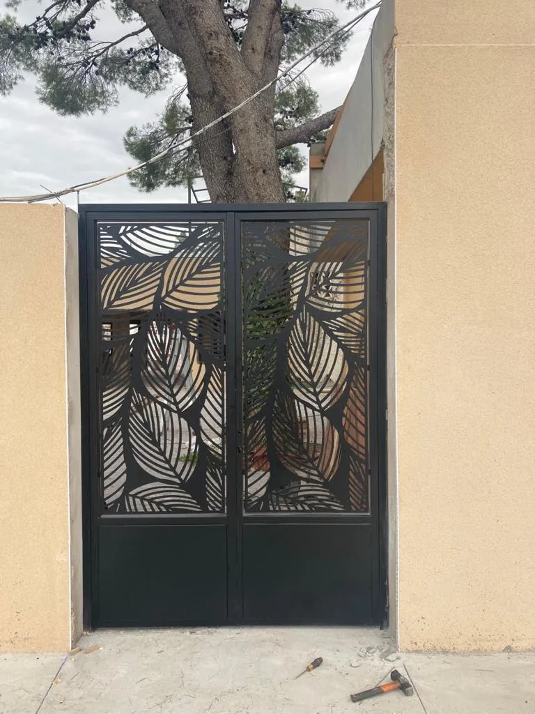 Puerta de hierro negra con diseño decorativo de hojas recortadas.