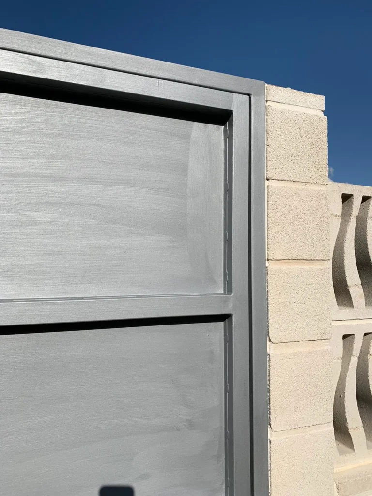 Detalle de puerta metálica gris con acabado cepillado y muro de bloques.