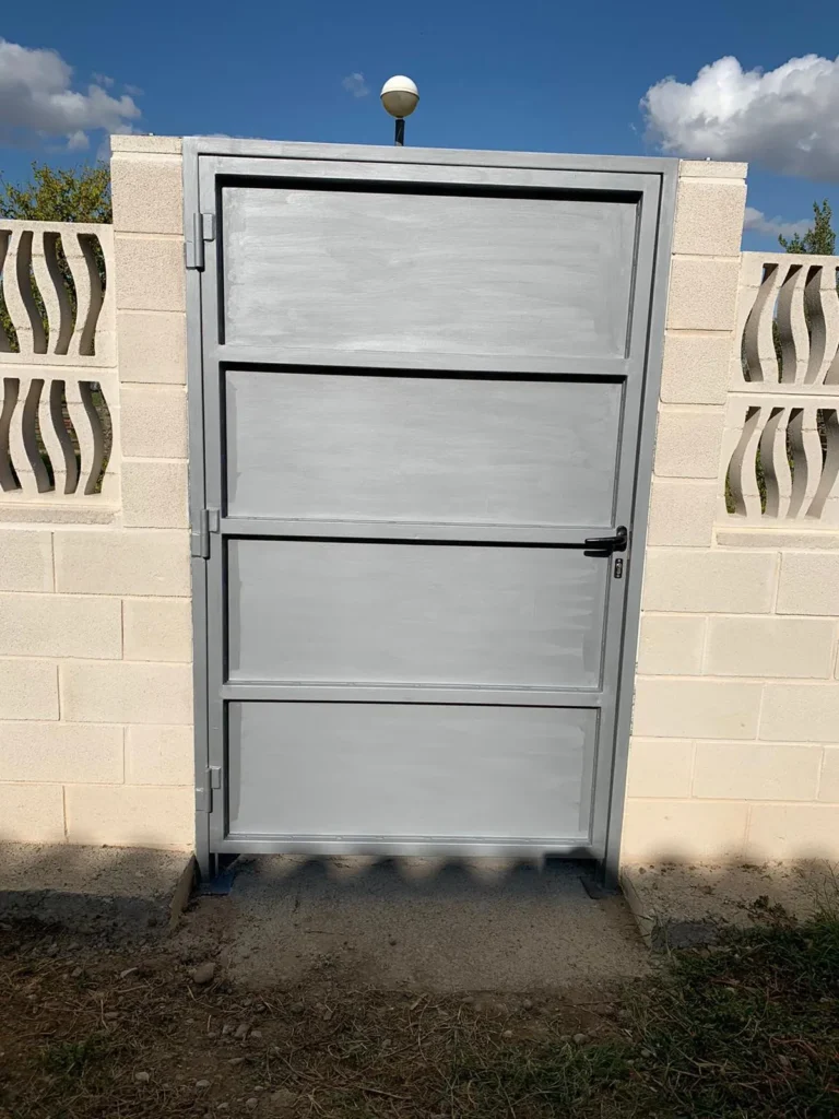 Puerta metálica gris vista frontalmente, cerrada con manilla negra