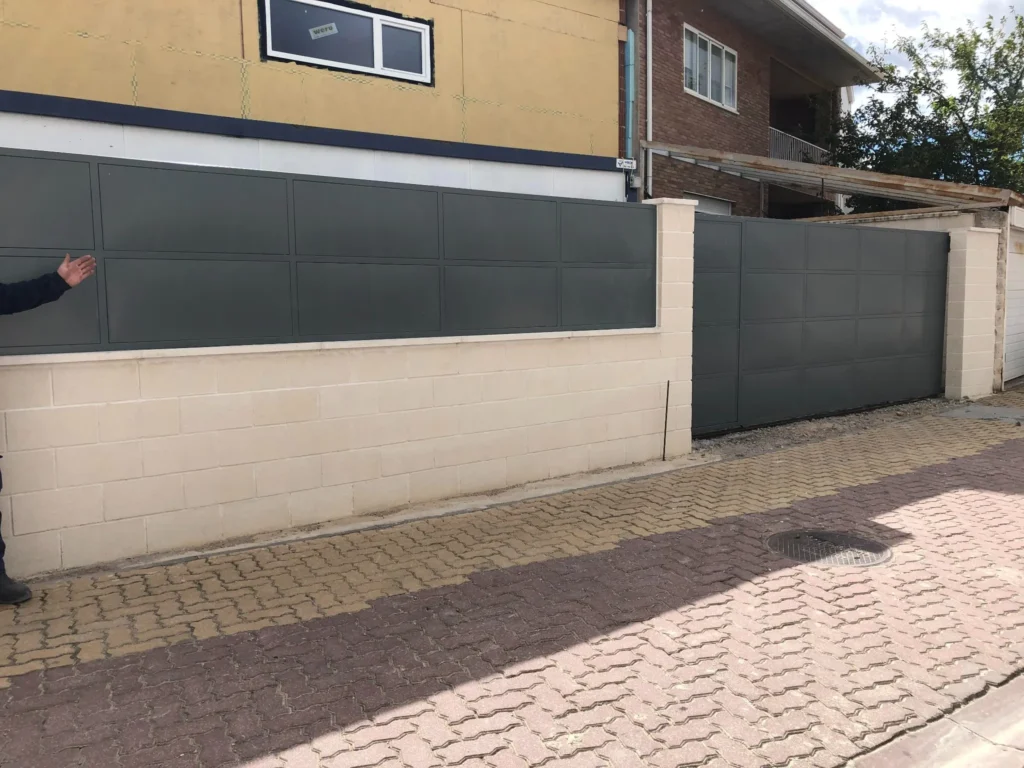 Persona señalando muro con paneles metálicos gris oscuro junto a puerta