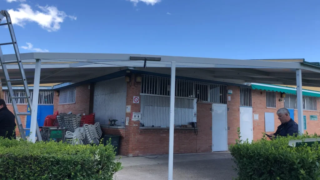 Marquesina blanca instalada sobre acera frente a edificio de ladrillo con sillas apiladas