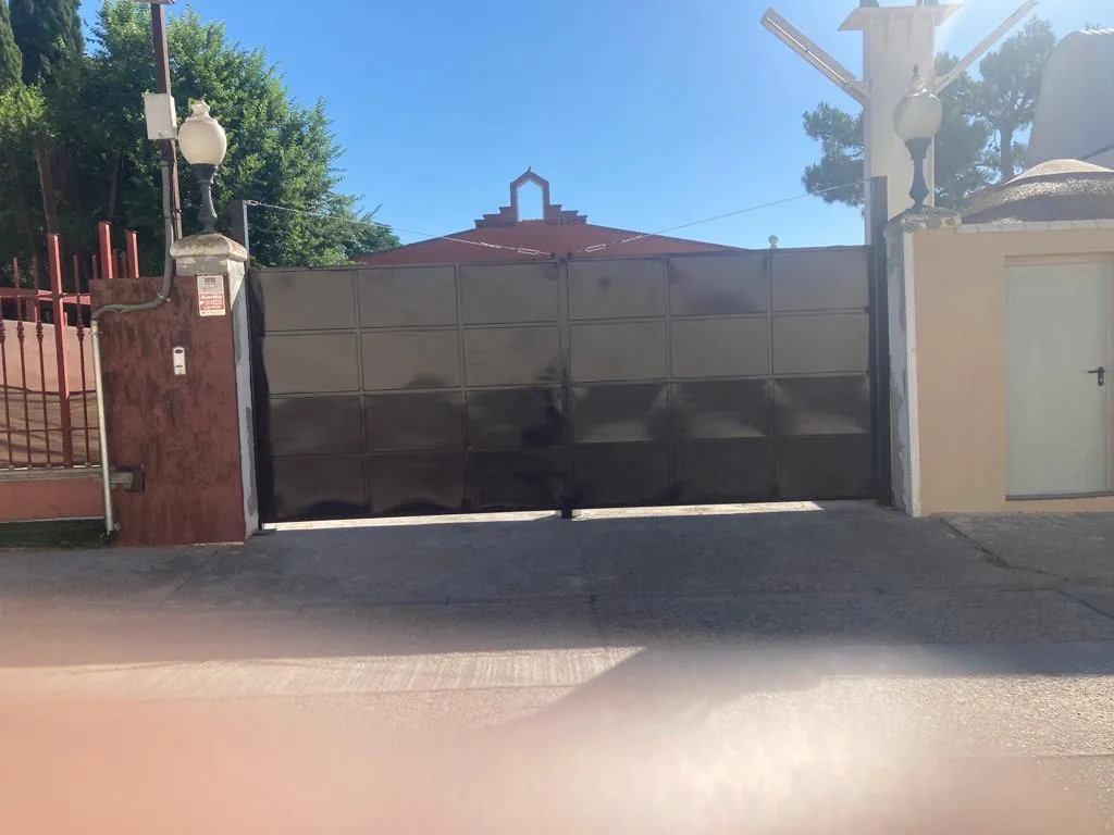 Portón metálico negro de dos hojas abatibles, en entrada de recinto