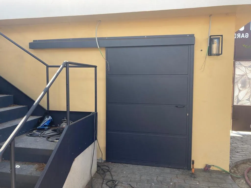 Puerta corredera metálica negra instalada bajo escalera exterior