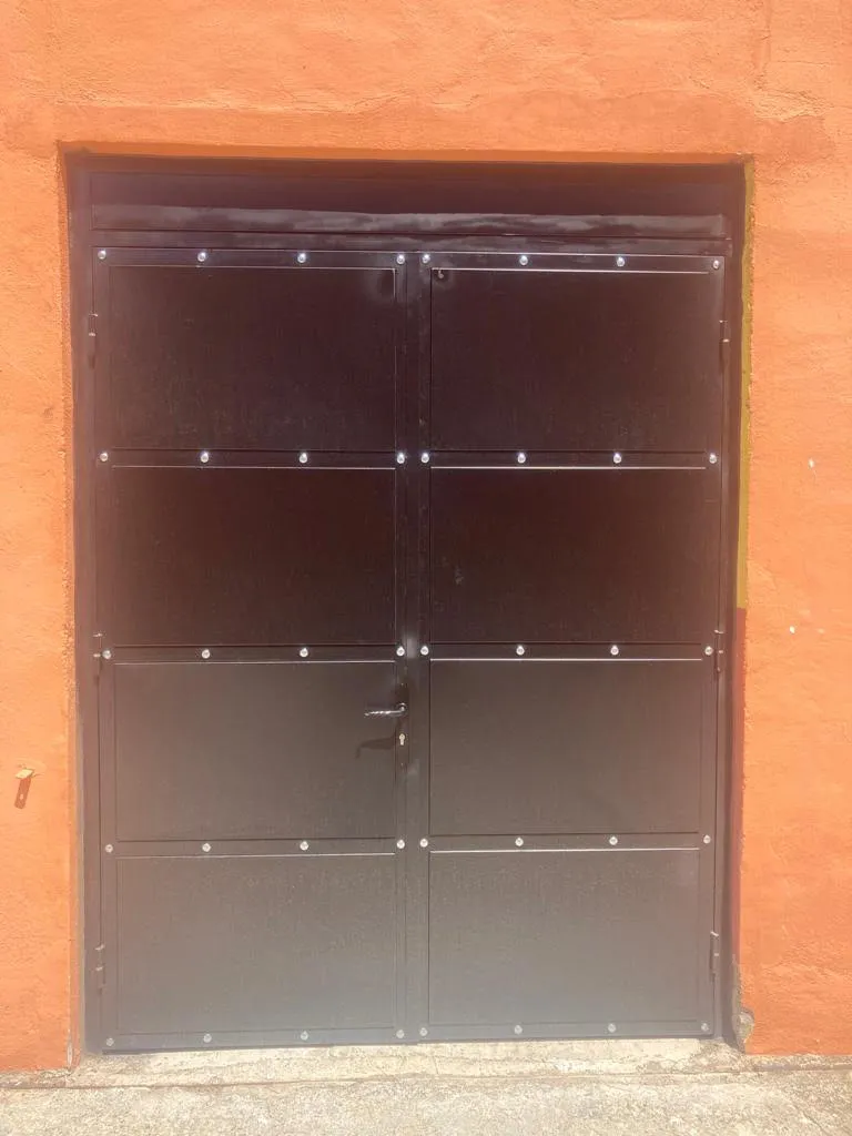 Detalle de portón abatible negro con remaches sobre fondo naranja