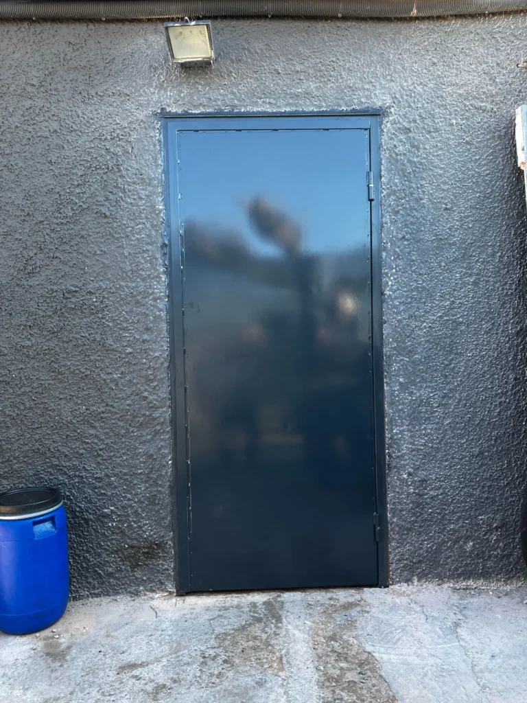 Puerta de chapa metálica lisa pintada de negro, instalada en un muro rugoso