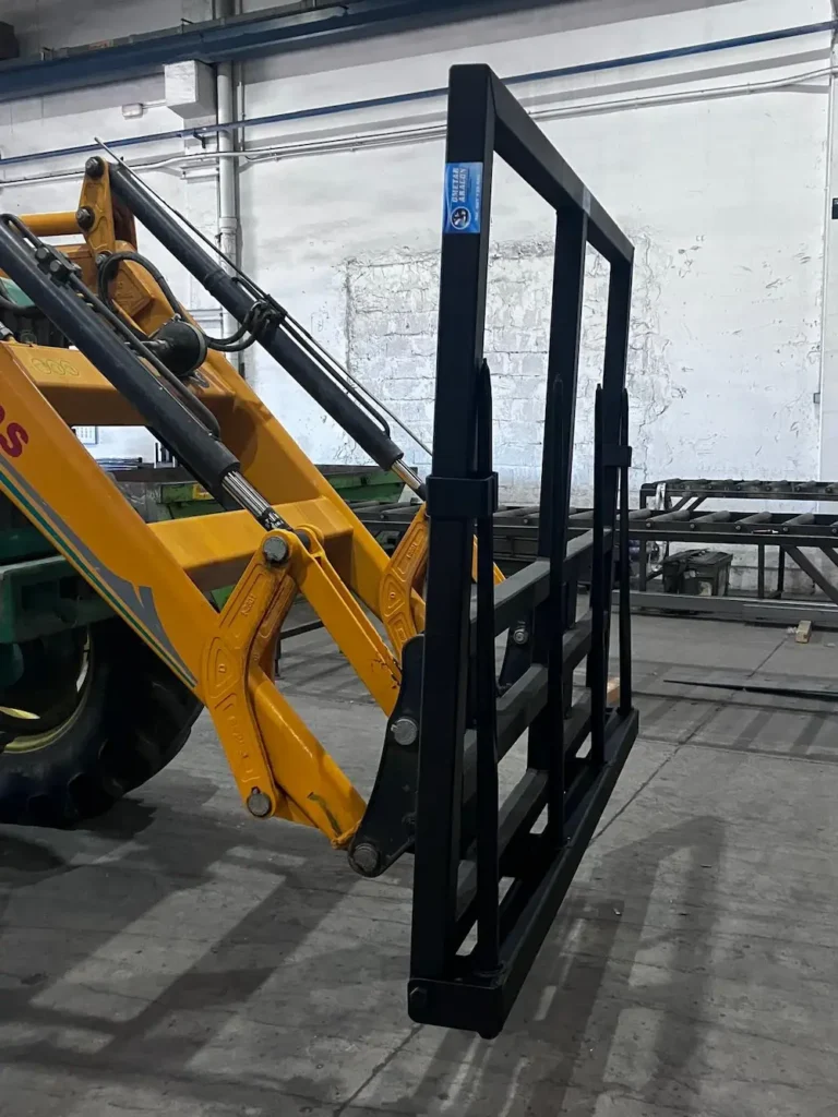 Vista lateral de una maquinaria amarilla levantando una estructura metálica negra dentro de un taller